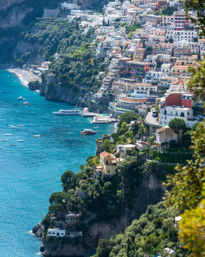 Colorful coastal village on cliffs with yachts blue sea and lush trees waterfront wallpaper background