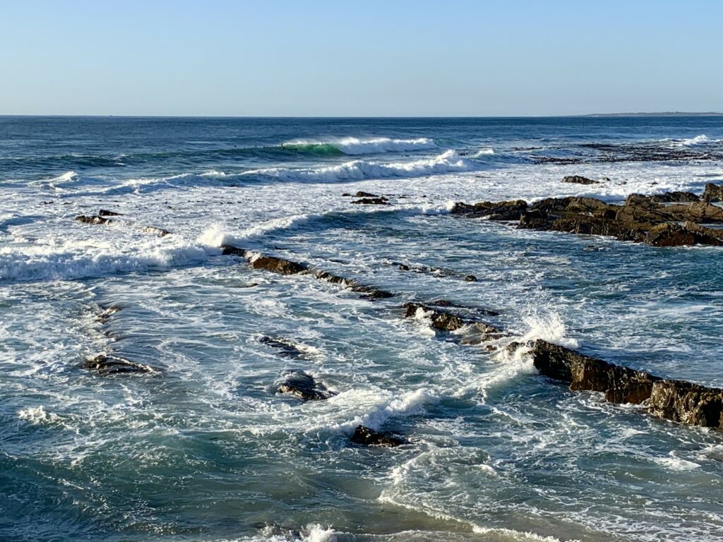 Coastal wallpaper with vibrant blue waves white foam and rugged rocky reefs under clear sky