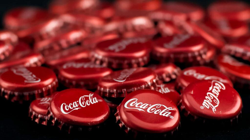 Close-up of glossy red Coca-Cola bottle caps wallpaper with iconic logo vibrant and high contrast