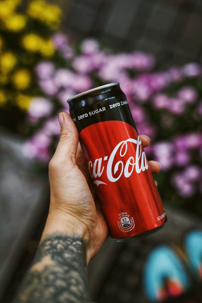Tattooed hand holding vibrant Coca-Cola Zero Sugar can with colorful yellow and pink flowers background Wallpaper