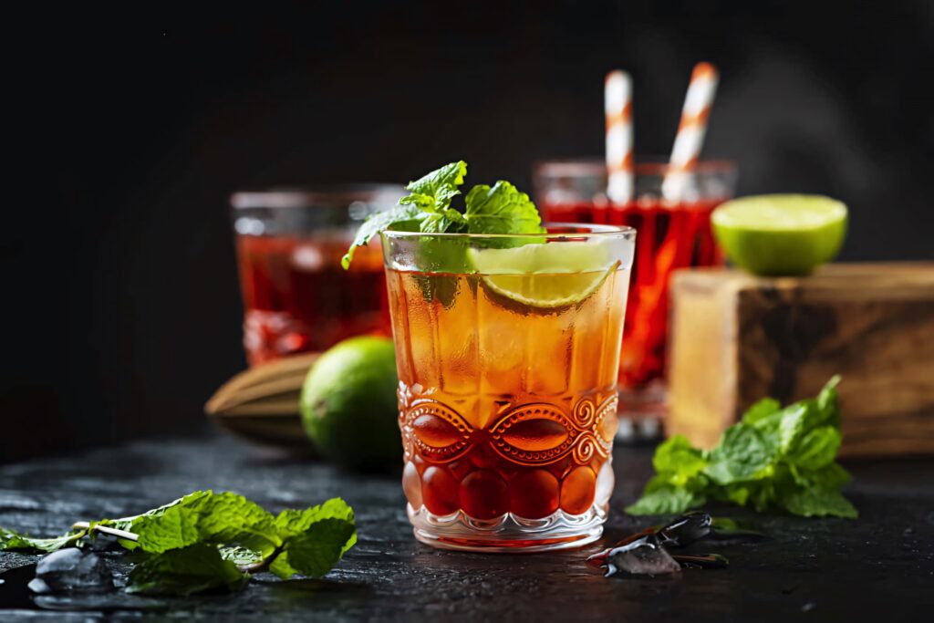 Vibrant cocktail with lime wedge and mint surrounded by herbs on dark textured table background Wallpaper