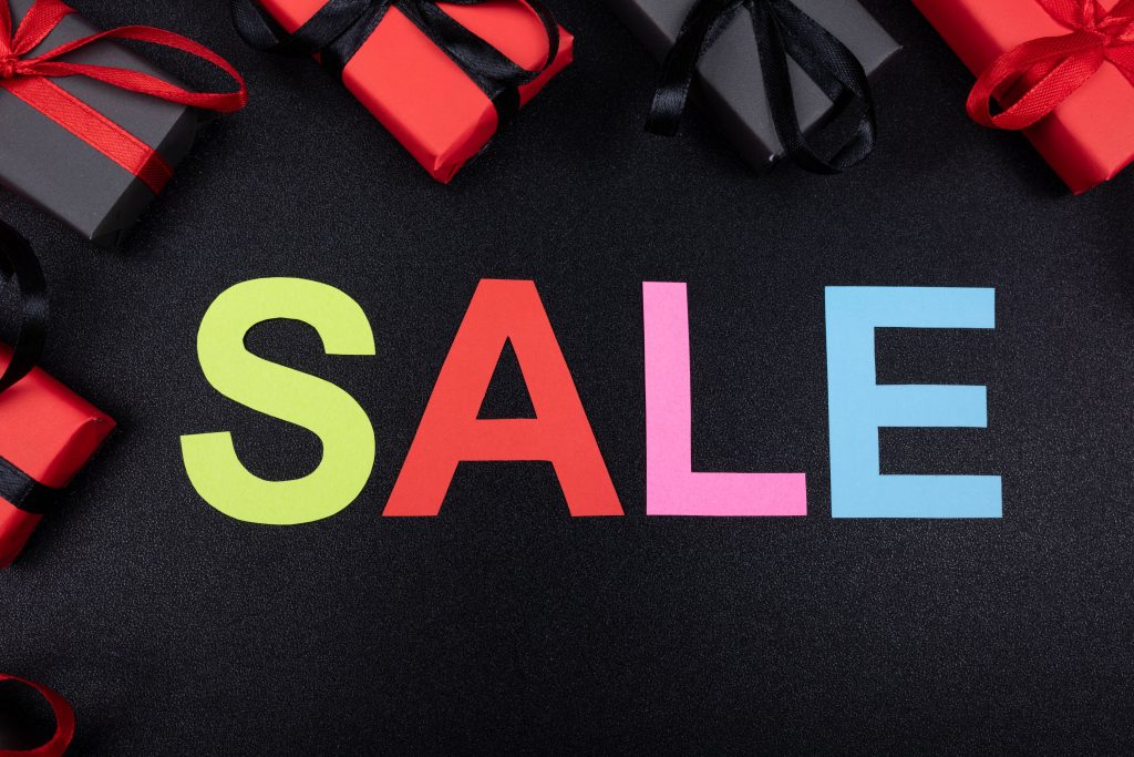 Vibrant SALE ad with colorful block letters and festive gift boxes on textured black background Wallpaper