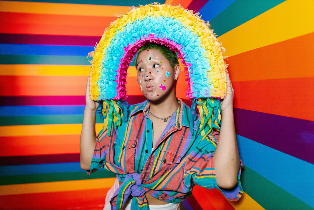 Vibrant Image: Woman Grasping a Rainbow Piñata amidst a Kaleidoscope Background Wallpaper