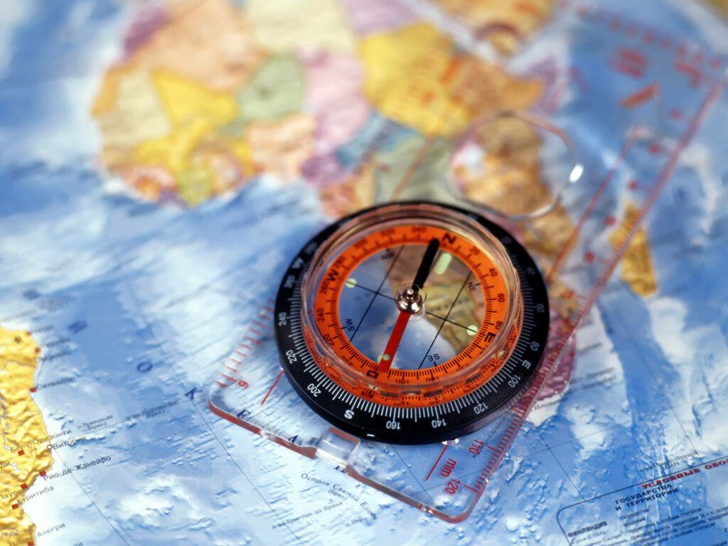 Detailed compass on colorful world map with vivid blues and oranges symbolizing navigation and exploration Wallpaper