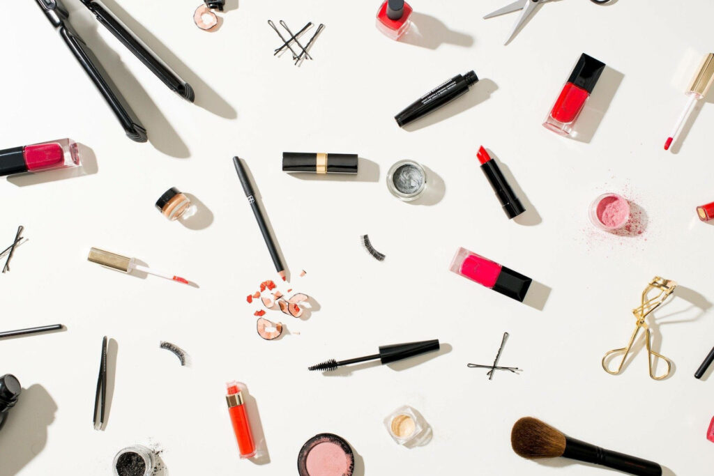 Vibrant cosmetics flat lay with lipsticks nail polish mascara brushes and hair tools on white background Wallpaper