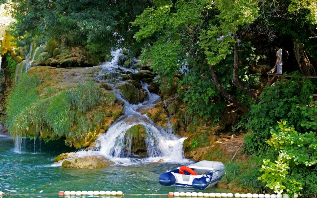 Inflatable boat near lush riverside and waterfalls in Croatia with tourists exploring nature Wallpaper