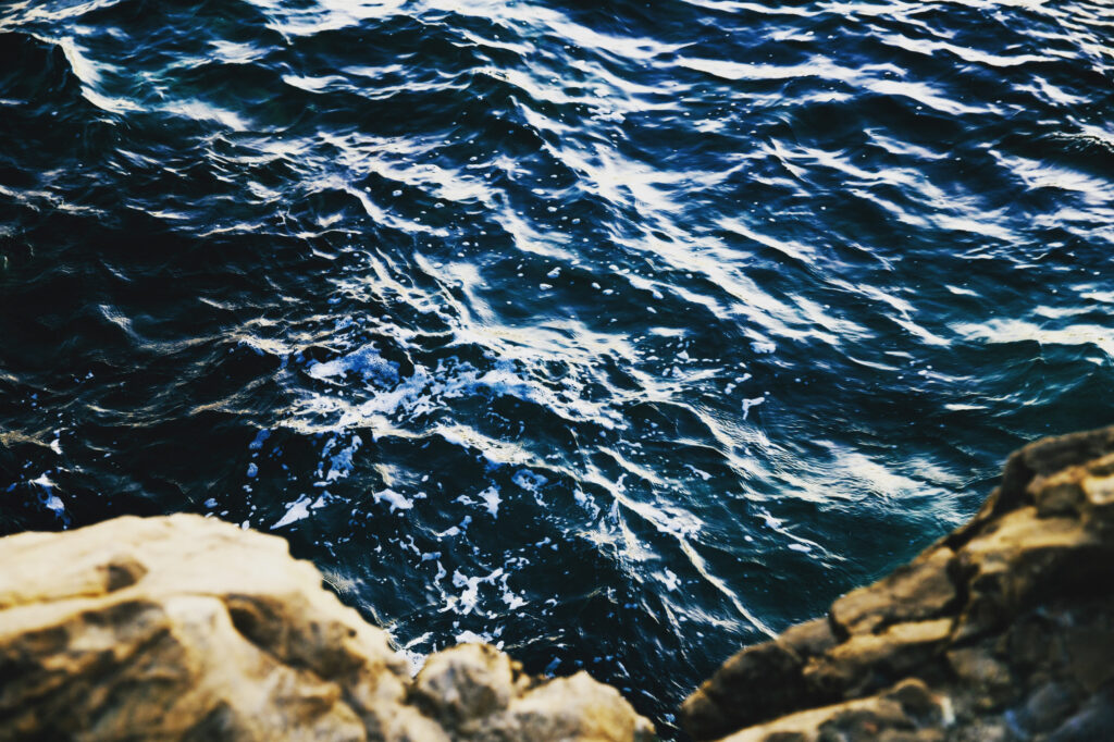 Vibrant deep blue sea waves crashing against rugged rocky shore in high contrast wallpaper