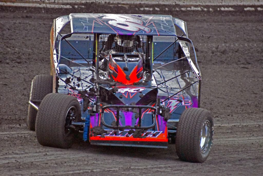 Vibrant dirt car with red and purple accents racing on rugged dusty track background wallpaper