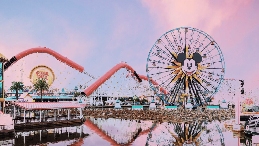Disneyland Ferris Wheel with Mickey Mouse face at pastel sunset reflecting colorful rides in water Wallpaper