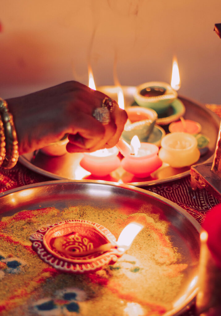 Diwali wallpaper with glowing clay diyas on metal tray rangoli patterns festive lighting hands