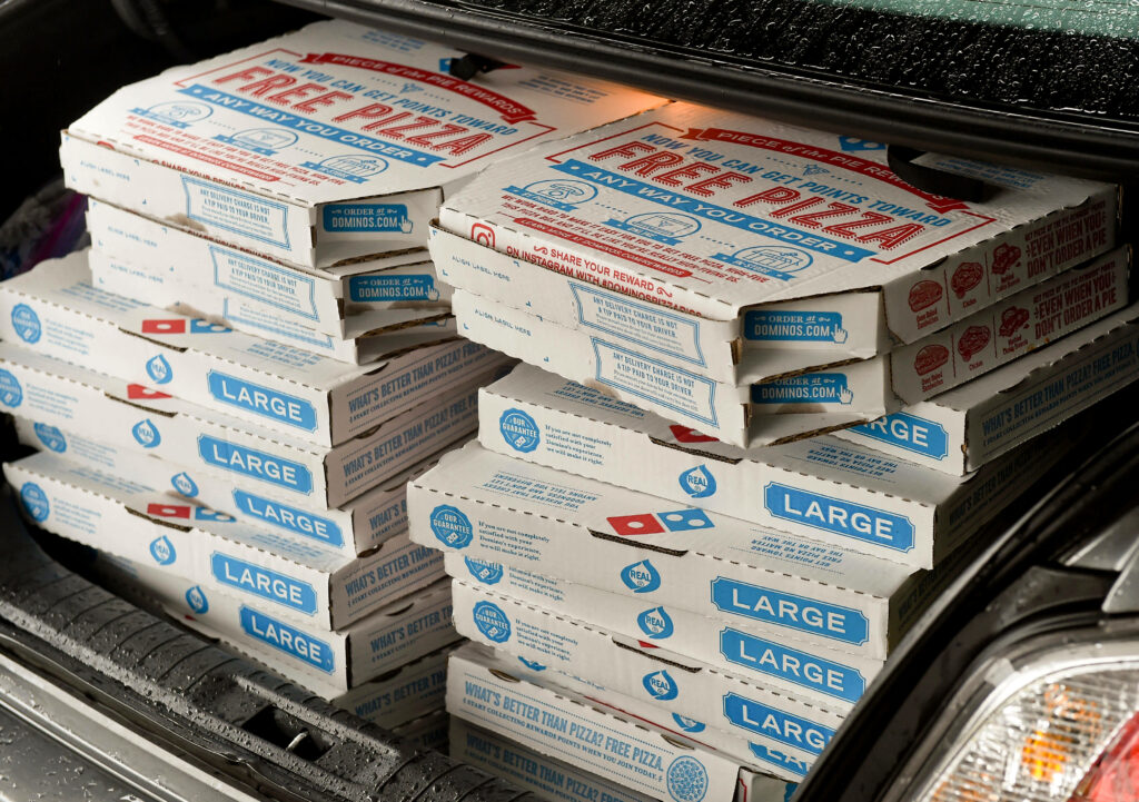Stacks of Domino’s Pizza boxes with iconic blue and red logo in car trunk wallpaper background