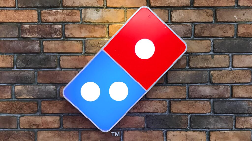 Dominos Pizza logo on rustic brick wall vibrant red and blue colors urban textured backdrop wallpaper