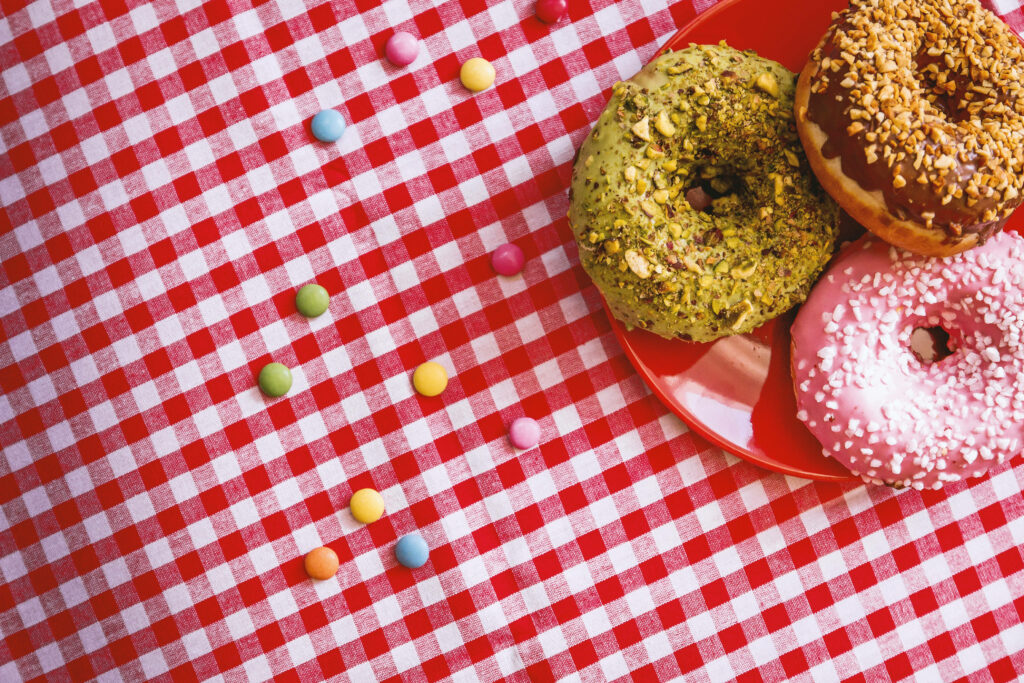 Vibrant donut wallpaper with three assorted colorful donuts on red plate checkered tablecloth