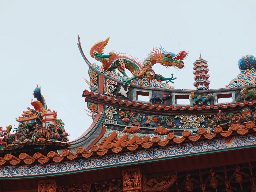 Dragon statue on ornate Chinatown temple rooftop with bold red gold carvings and clear sky background Wallpaper