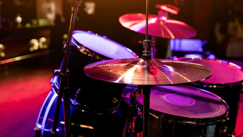 Close-up of a vibrant drum set with shining cymbals under colorful purple red and gold stage lights Wallpaper