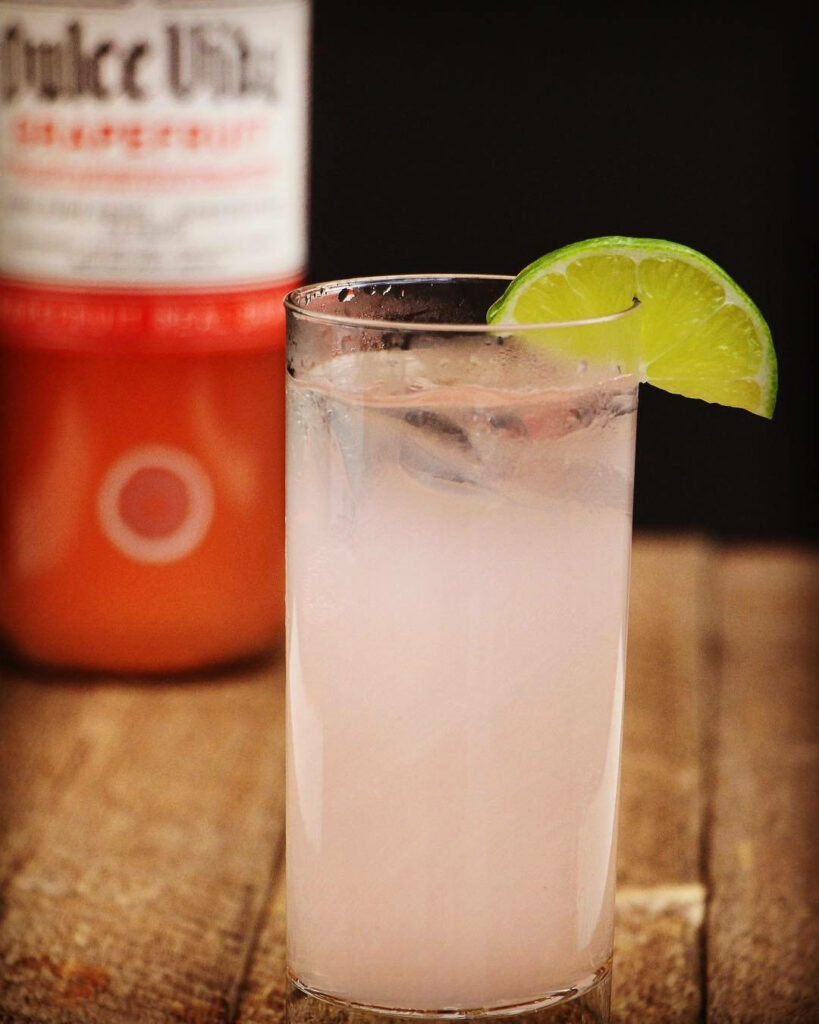 Refreshing Dulce Vida Grapefruit Tequila cocktail with lime on rustic table and blurred bottle background Wallpaper