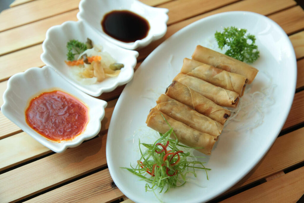 Egg roll platter with colorful dips on white plate and wooden table vibrant wallpaper background