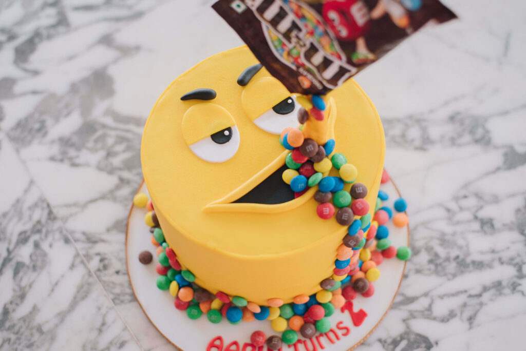 Vibrant emoji cake wallpaper with colorful M&Ms candy cascade smooth fondant dessert design