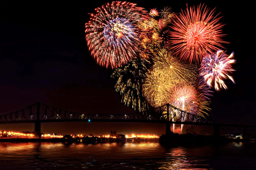 Vibrant fireworks explode over illuminated bridge reflecting on calm water at night wallpaper background