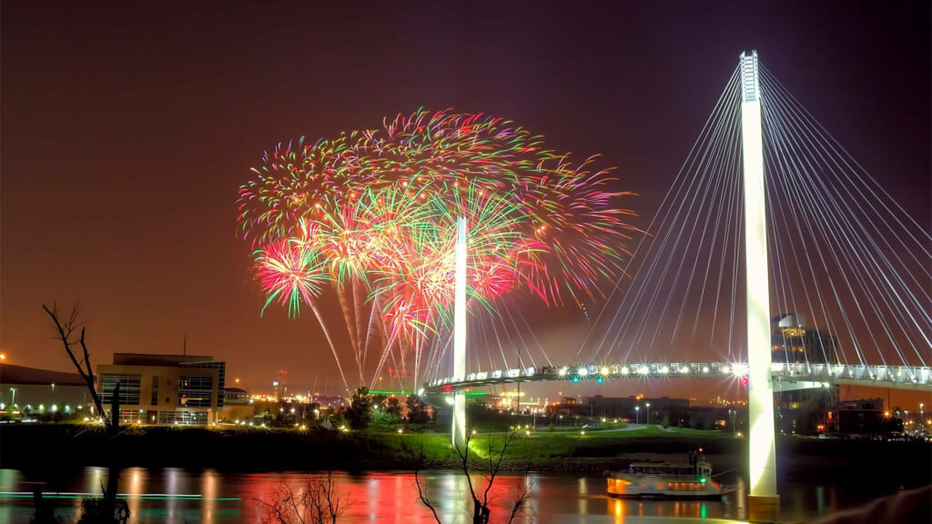 Fireworks illuminate night sky over Missouri cable-stayed bridge reflecting colorful lights on water Wallpaper