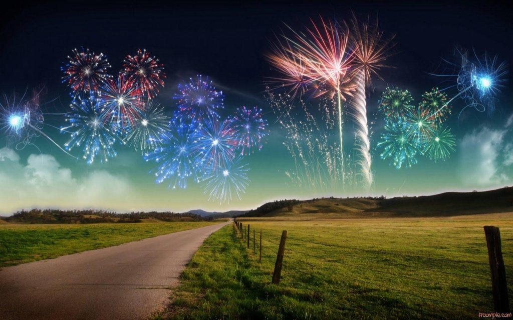 Vibrant fireworks lighting colorful night sky over peaceful rural landscape with winding road Wallpaper
