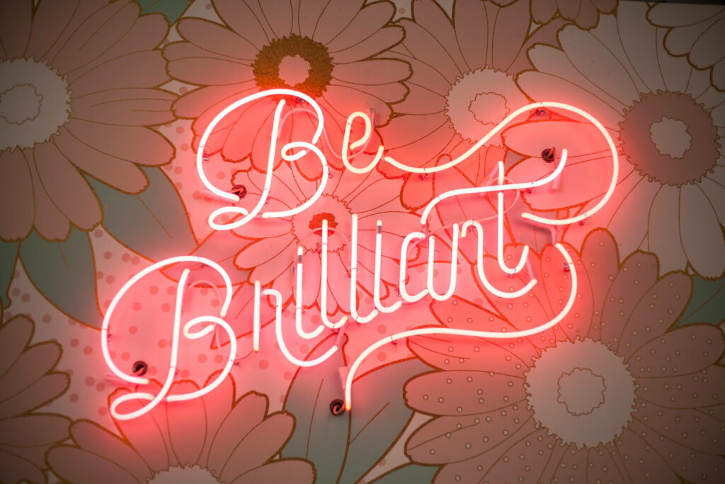 Vibrant Floral Wallpaper with Pink Neon 'Be Brilliant' Sign