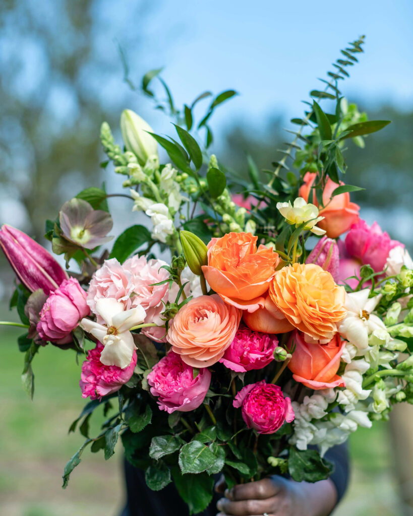Vibrant Mixed Flower Bouquet Against Greenery & Blue Sky Wallpaper