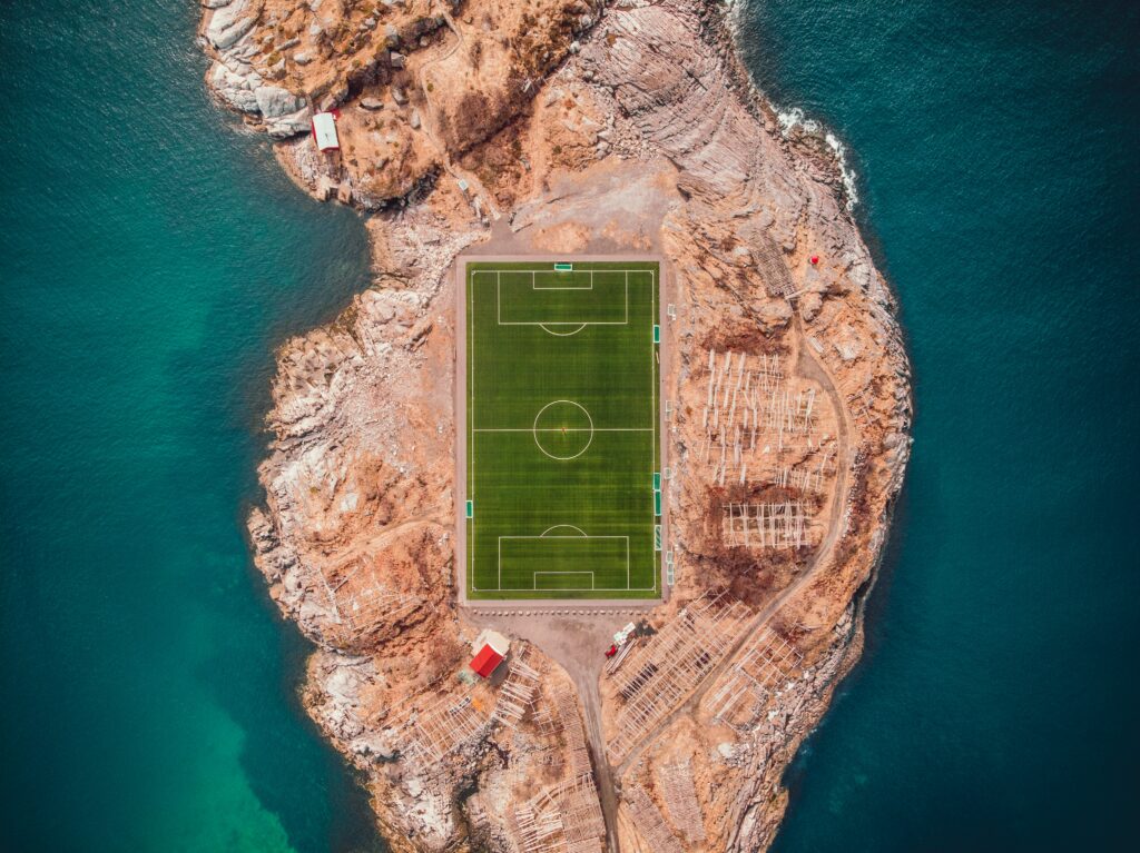 Top-down vibrant football field on rugged Lofoten island Norway surrounded by blue waters wallpaper