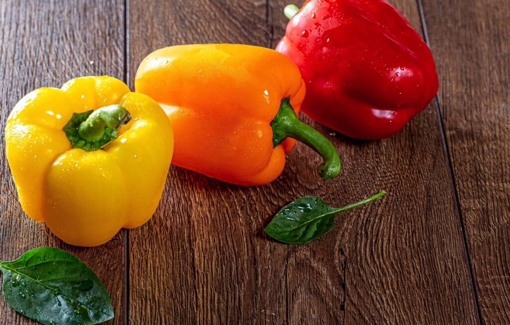 Top view of fresh yellow orange red bell peppers on rustic wooden surface wallpaper background