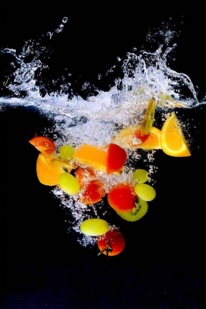 Colorful fresh tomatoes orange slices green grapes splash into clear water black background wallpaper