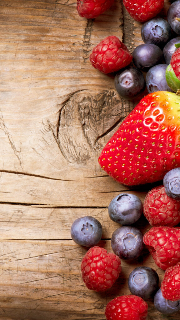 Vertical wallpaper with fresh raspberries blueberries and juicy strawberry on rustic wood