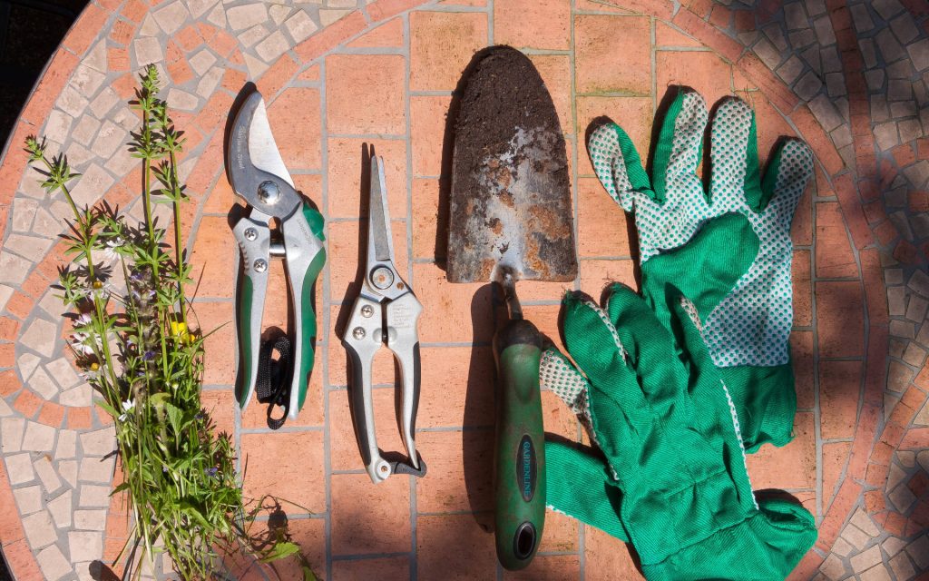 Top-down view of garden tools gloves and wildflowers on terracotta mosaic floor gardening wallpaper