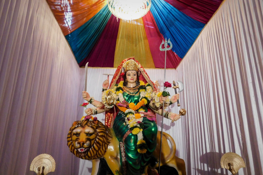 Vibrant statue of Hindu Goddess Durga on lion with colorful garlands and rich curtain backdrop Wallpaper