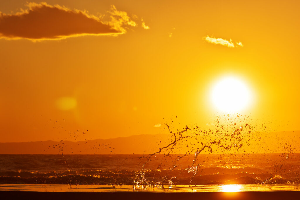 Vibrant sunset over sea with golden sky sunlight reflections and dynamic sea spray wallpaper background