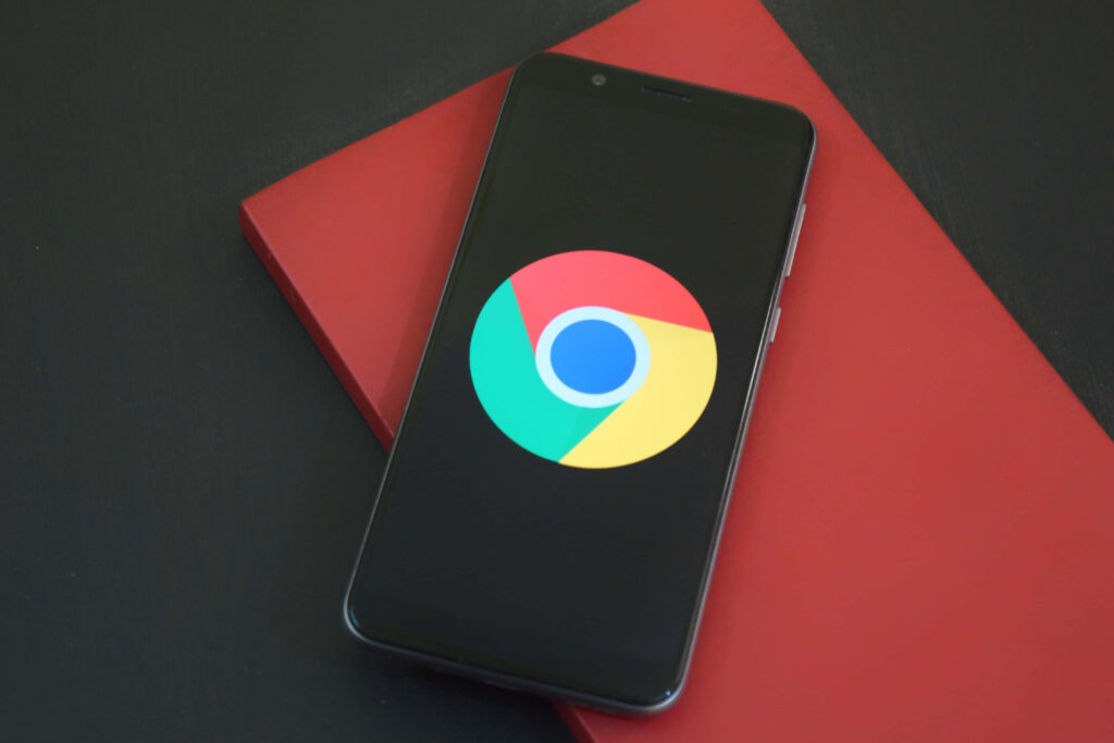 Smartphone showing vibrant Google Chrome logo on black screen on red notebook with dark background Wallpaper