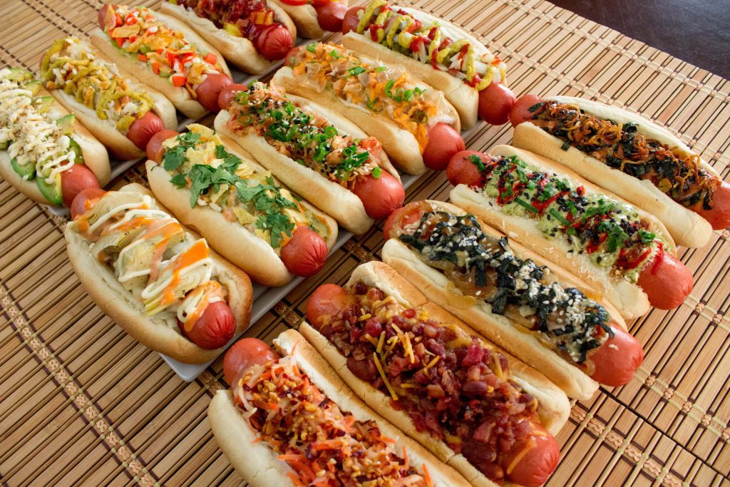 Gourmet hot dogs with colorful toppings on bamboo mat vibrant high-angle food wallpaper background