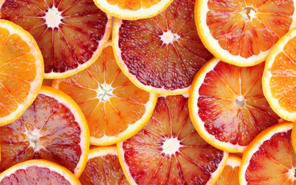 Vibrant wallpaper of thinly sliced grapefruits in red orange and yellow gradient fresh background