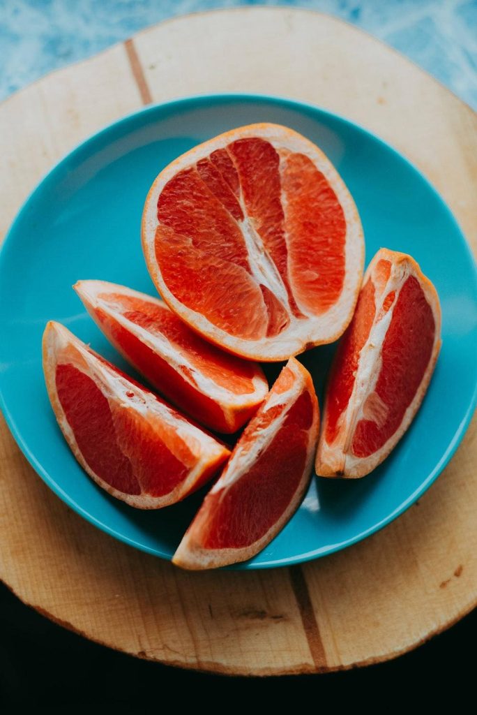 High-angle photo of vibrant grapefruit slices on blue plate with rustic wooden background wallpaper