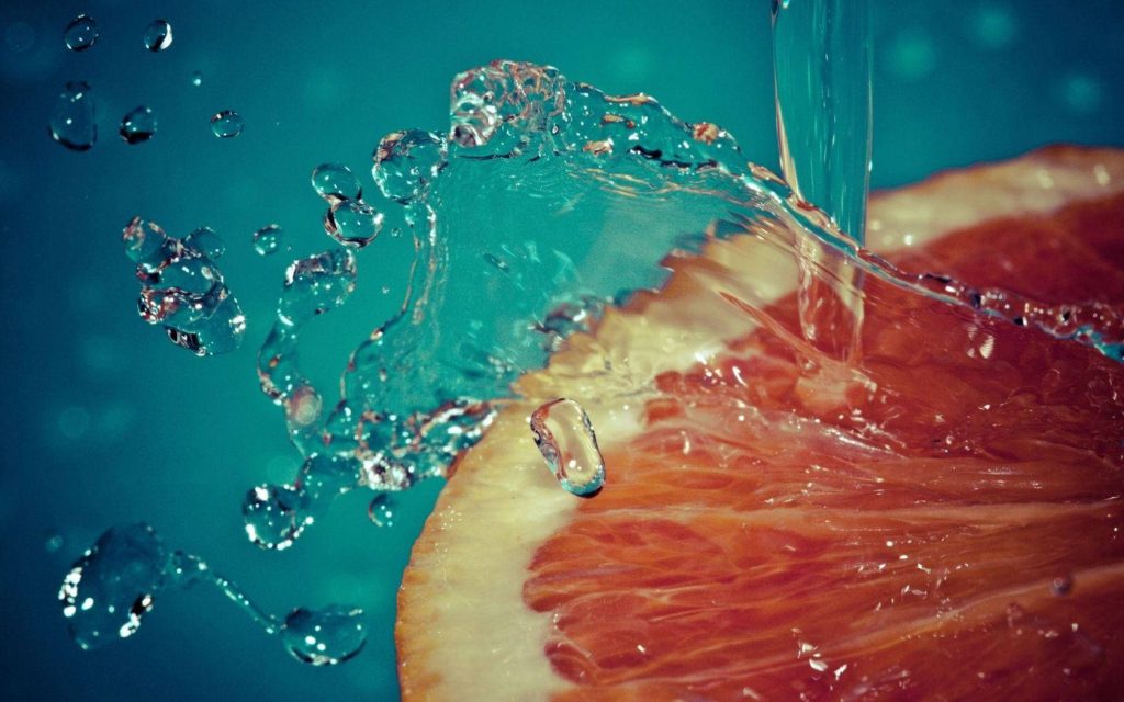 Vibrant grapefruit slice splashing in clear water with turquoise background high-speed wallpaper