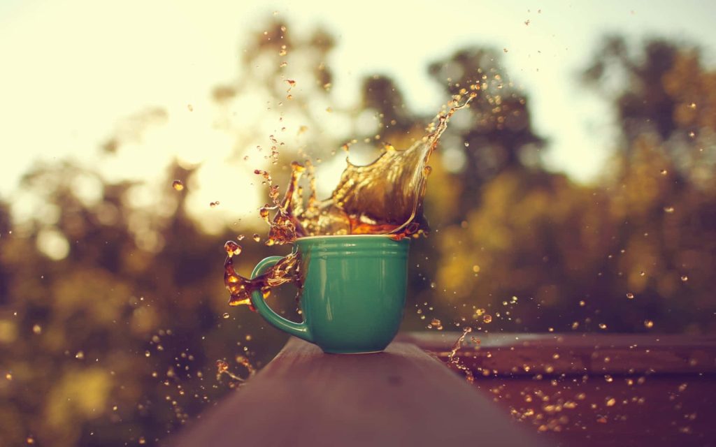 Vibrant green coffee mug with mid-air coffee splash in warm sunlight nature background wallpaper