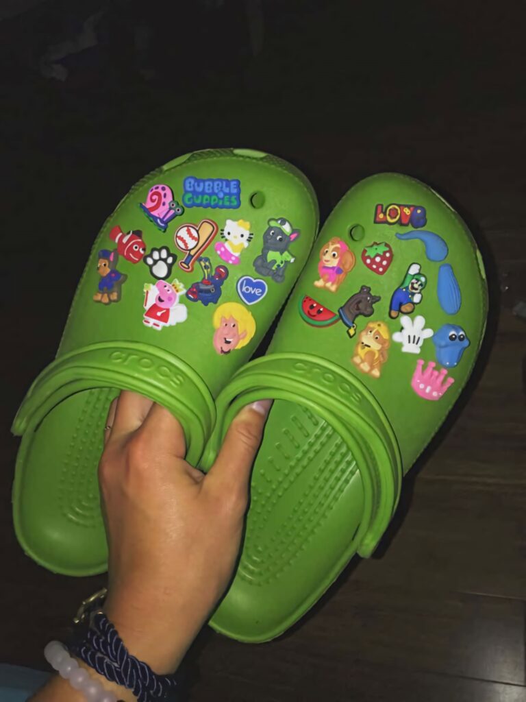 Vibrant green Crocs with colorful cartoon charms held in hand showcasing customizable fun style Wallpaper
