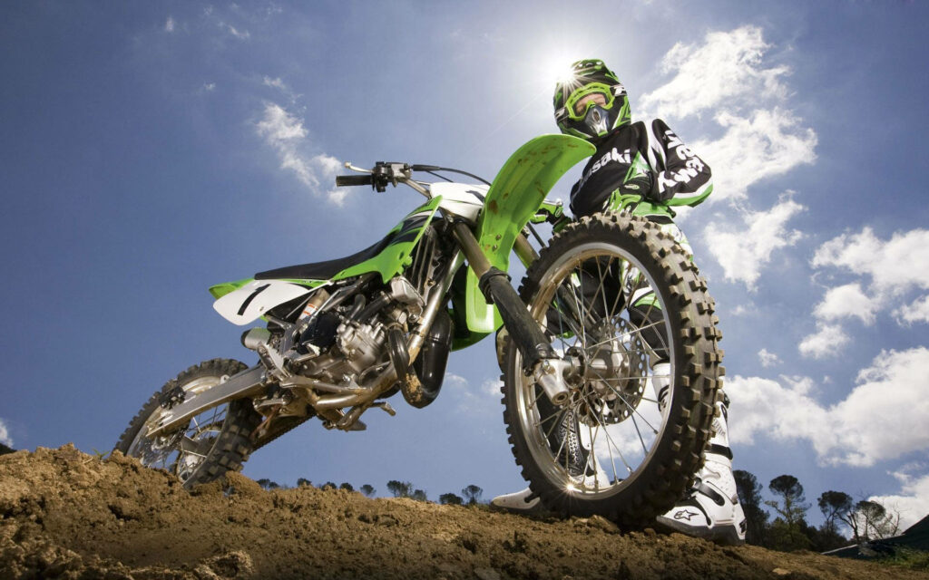 Vibrant Green Dirt Bike Wallpaper on Rugged Terrain Under Blue Sky