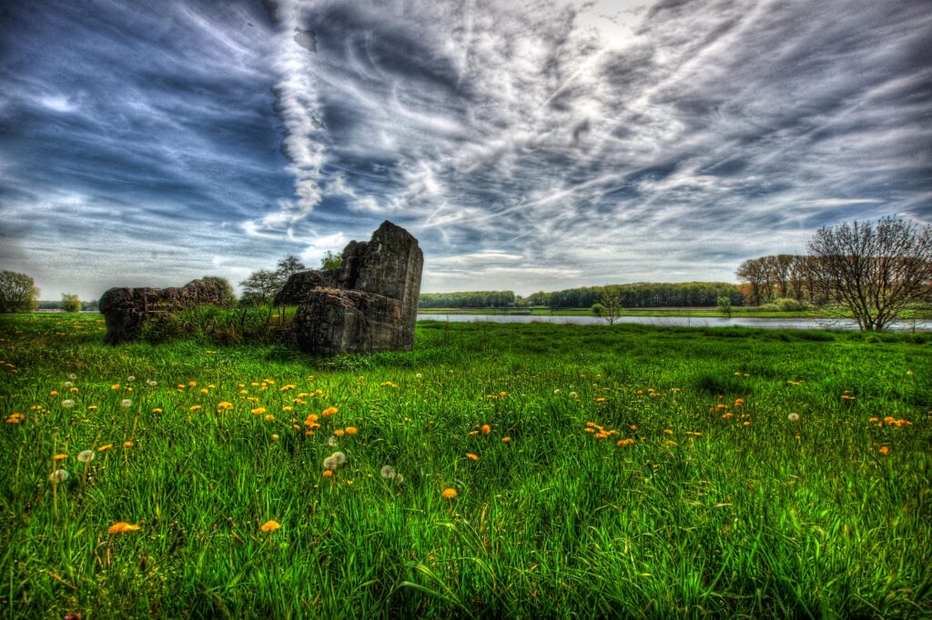 Lush green field with dandelions river reflecting dramatic clouds and weathered rocks wallpaper
