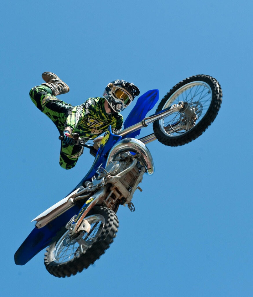 Dirt bike rider in green and black gear performing high aerial motocross stunt clear sky Wallpaper