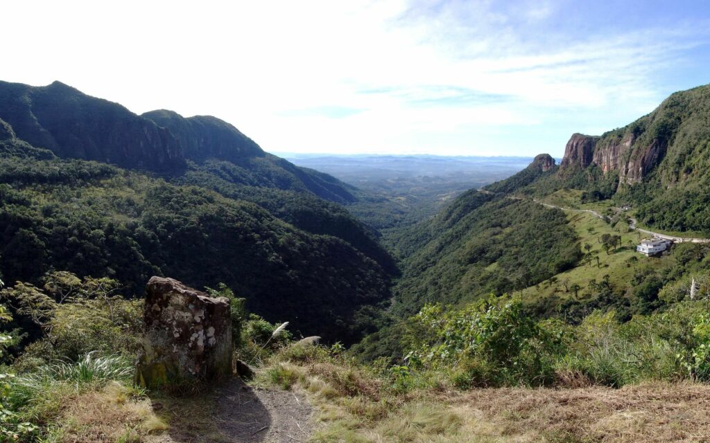 Vibrant green mountaintop overlooking lush valley rolling hills and cliffs under bright sky Wallpaper