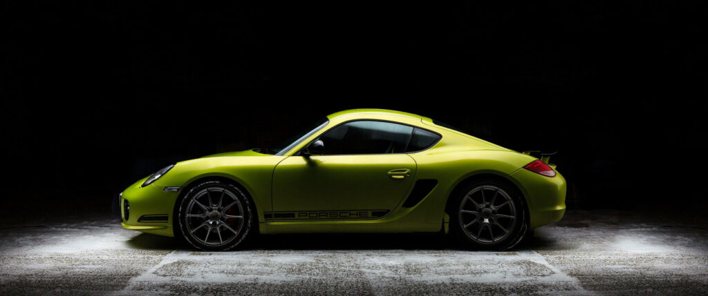 Vibrant green Porsche Cayman R with sleek curves under dramatic lighting on dark wallpaper background