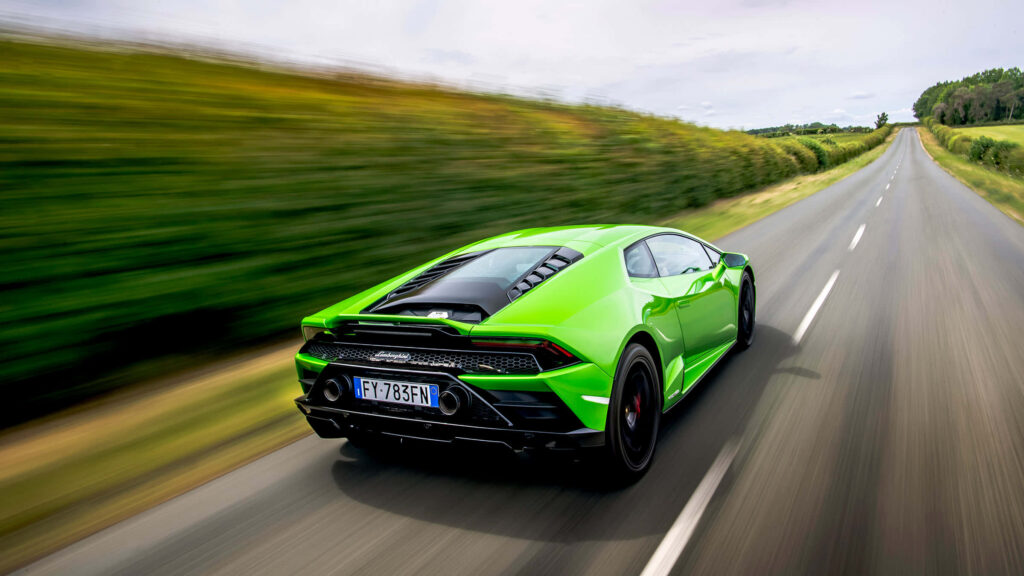 Vibrant green sports car racing on scenic country road with lush greenery and blue sky wallpaper