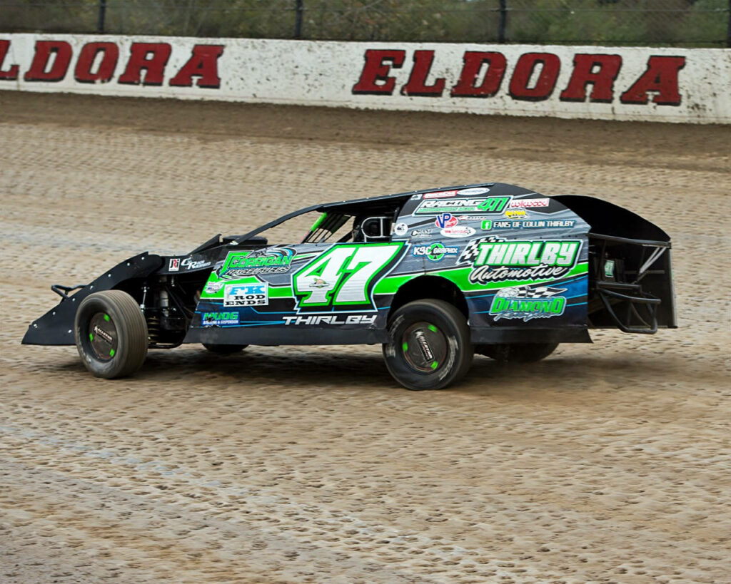 Green and black dirt race car speeding on sandy Eldora racetrack with bold sponsor logos Wallpaper