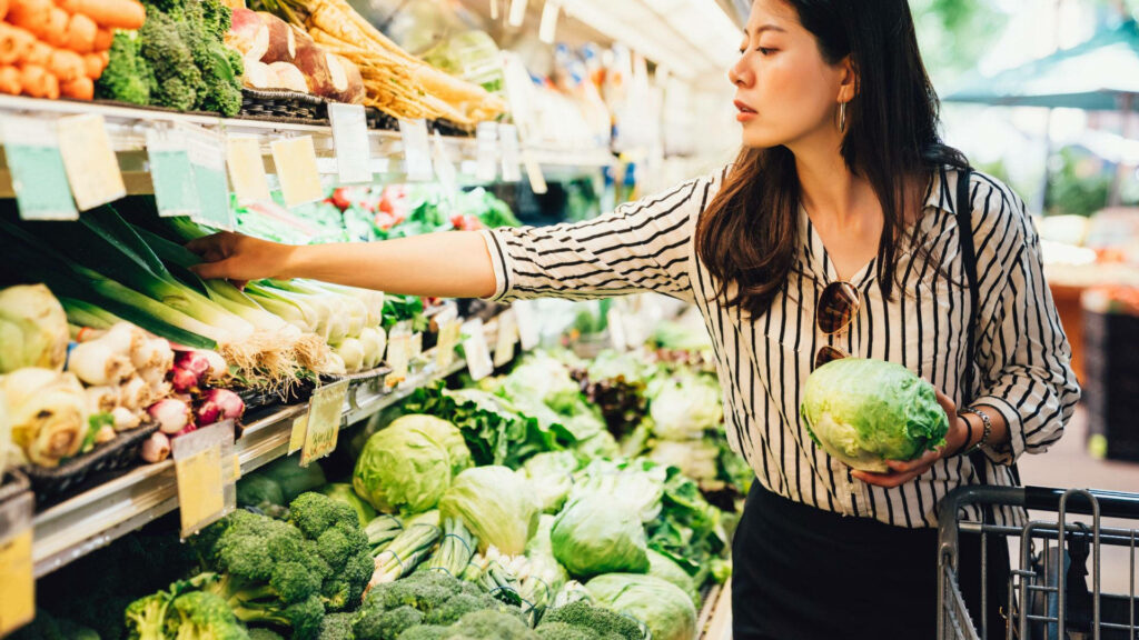 Vibrant Grocery Store Scene: Woman Choosing Fresh Vegetables Wallpaper