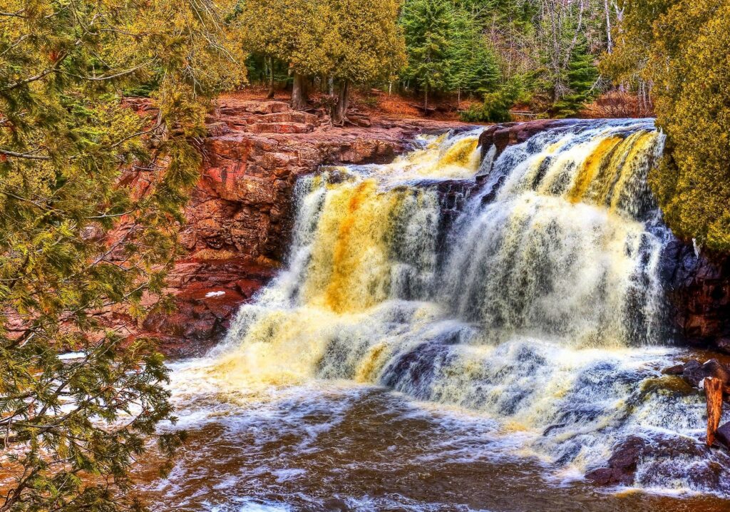 Vibrant HDR waterfall cascading over rocks surrounded by lush green forest and river landscape Wallpaper